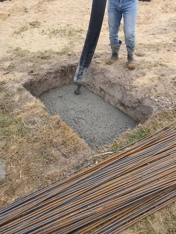 Concrete being poured into a footing next to a stack of rebar