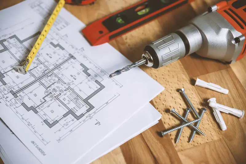 Floor plan on a table with a tape measure, a spirit level, a drill and screws