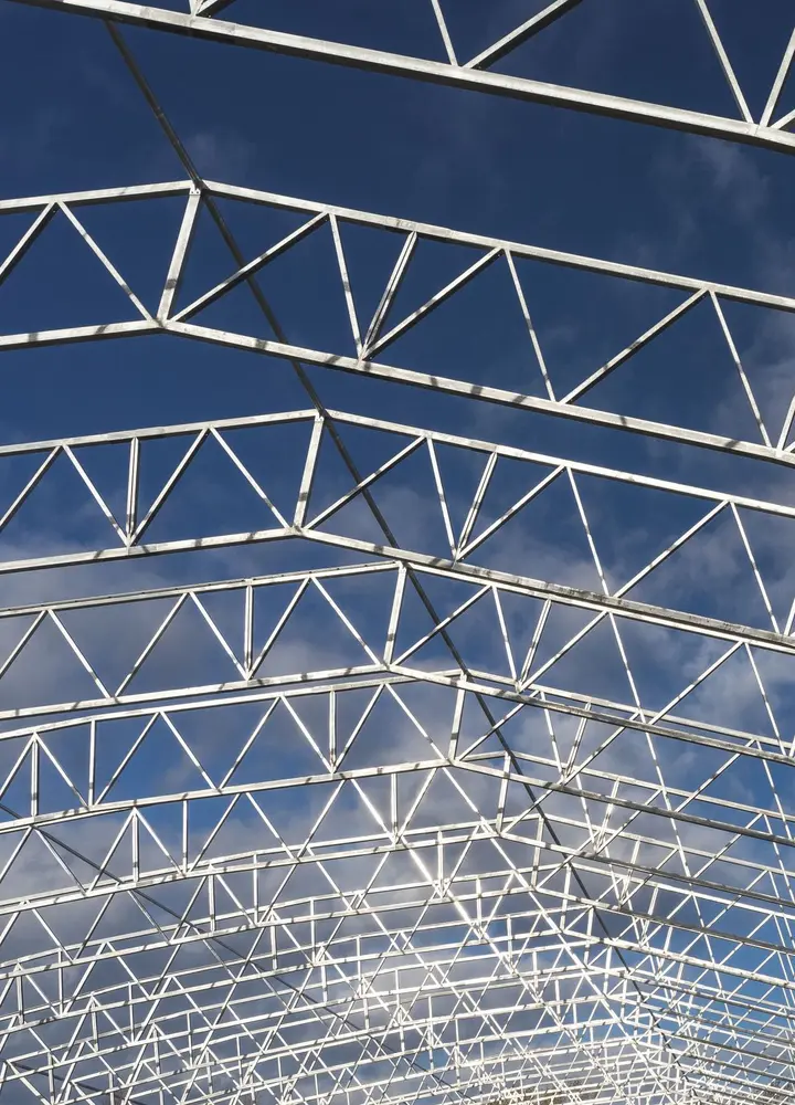 Steel roof trusses against a blue sky, seen from below